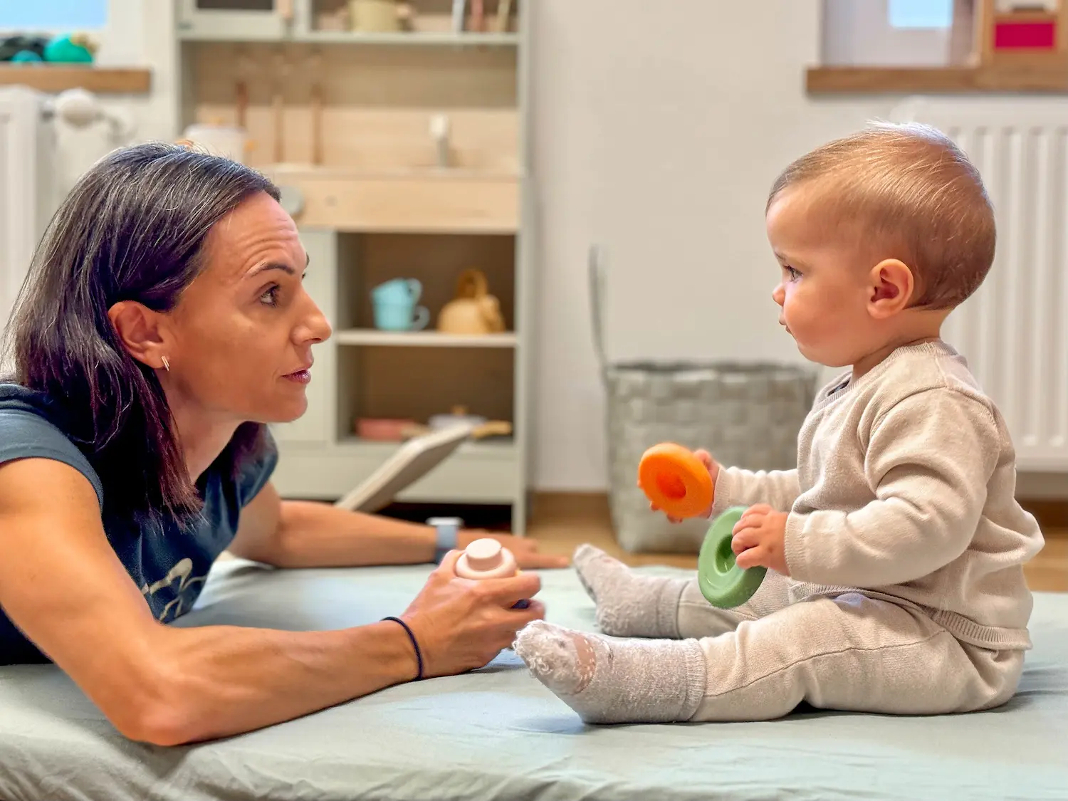 Dr. Martina Rinner interagiert auf Augenhöhe mit einem Kleinkind, das mit buntem Spielzeug spielt, und schafft eine sichere und anregende Umgebung zur Förderung der frühkindlichen Entwicklung.