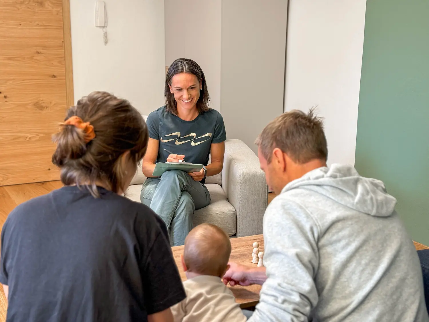 Dr. Martina Rinner im Gespräch mit einer Familie, die sich spielerisch mit ihrem Kleinkind beschäftigt; sie schafft eine offene und unterstützende Atmosphäre für die Familienberatung.