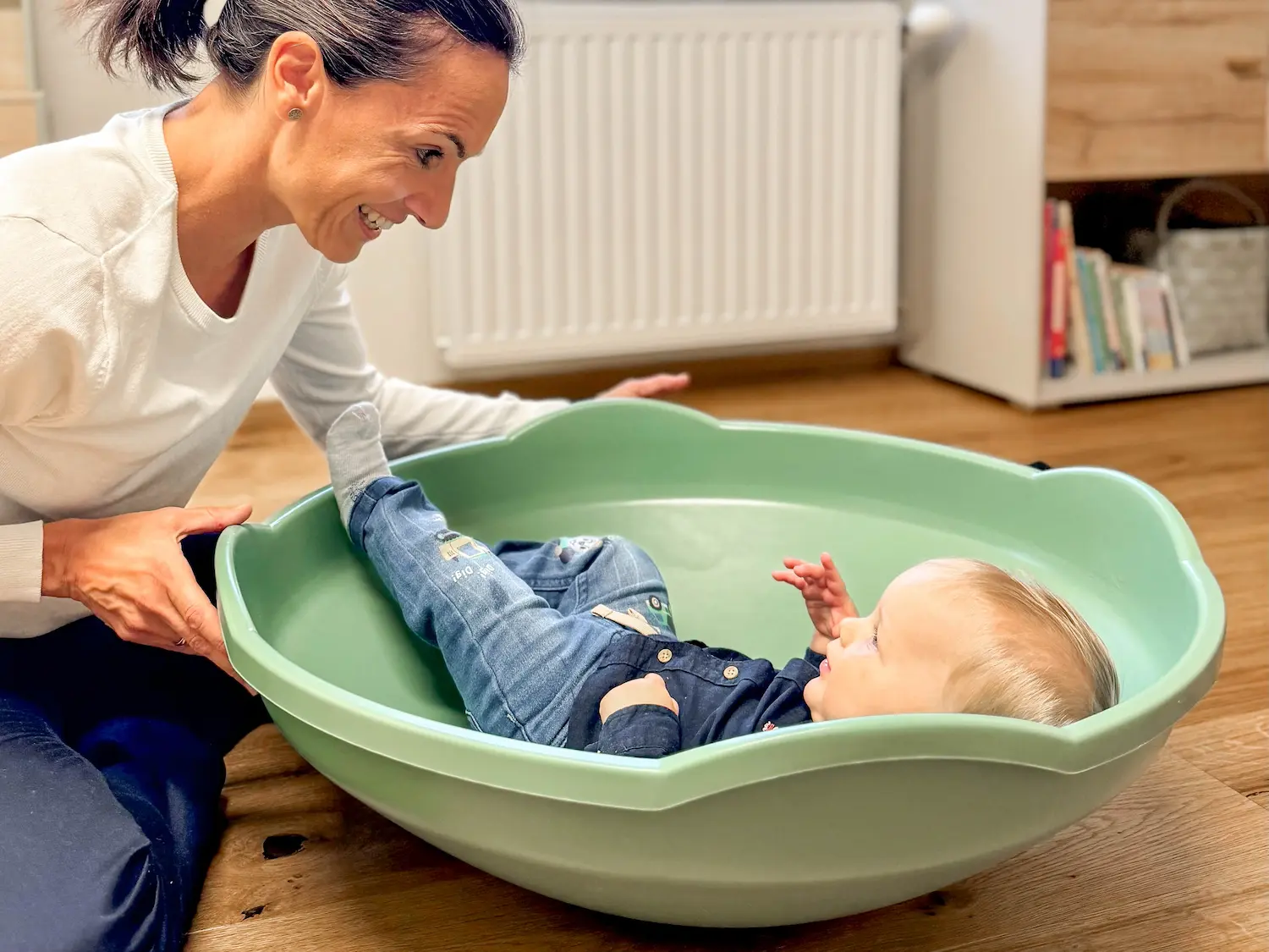 Dr. Martina Rinner dreht ein Kleinkind spielerisch in einem großen grünen Kreisel, um Freude und sensorische Wahrnehmung in einer sicheren Praxisumgebung zu fördern.